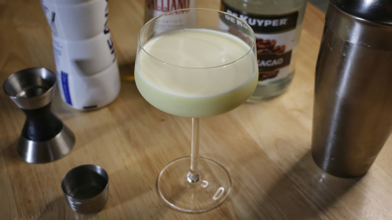 golden Cadillac cocktail on wooden table with liquor bottles and cocktail equipment