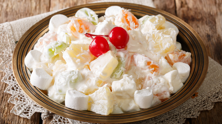 Ambrosia salad with pineapple, oranges, grapes and coconut with marshmallow and vanilla yogurt close-up on a plate
