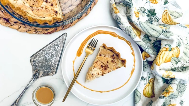 Slice of apple and custard pie on plate with autumn decorative cloth