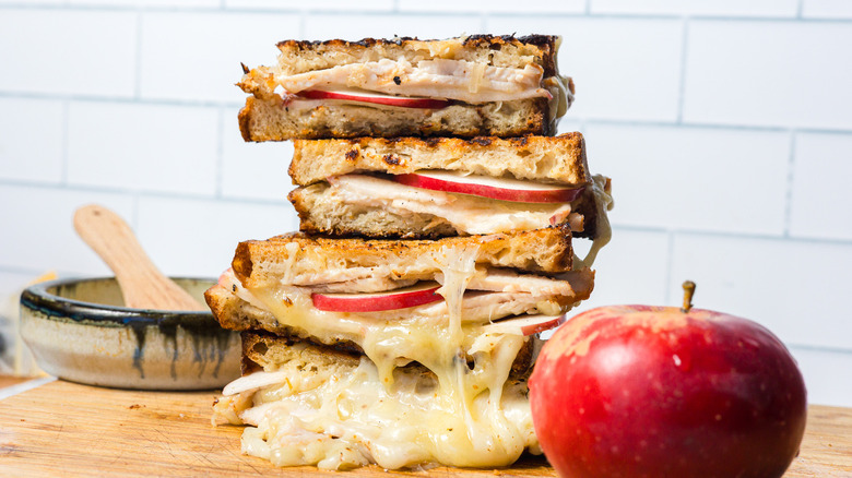 A stack of grilled apple turkey cheddar sandwiches with an apple in front of them