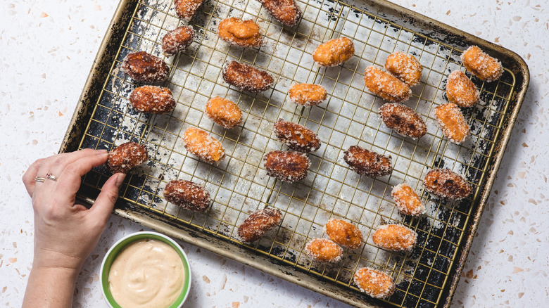 hand grabbing sweet potato tater tot from cookie sheet