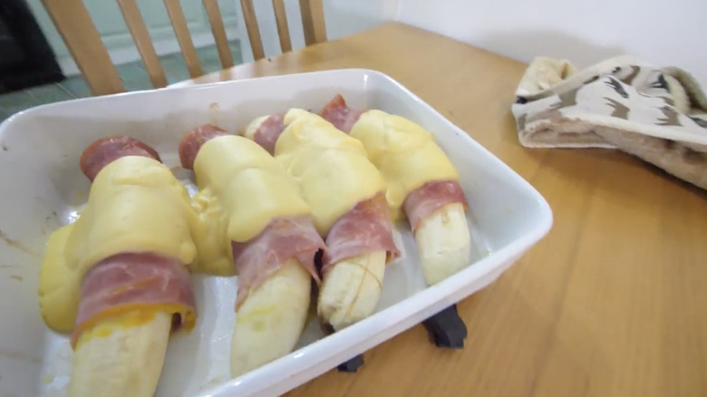 dish of bananas wrapped in bacon with hollandaise on kitchen table