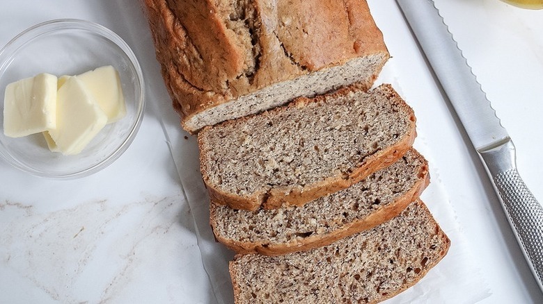 Sliced banana bread loaf next to knife and bowl of butter
