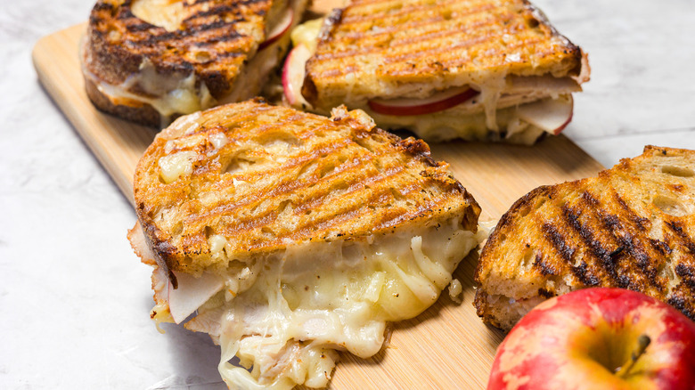 Four grilled apple turkey cheddar sandwich halves with an apple