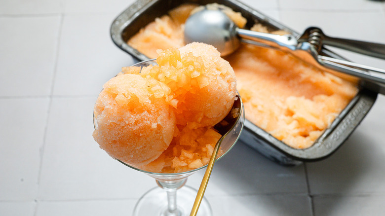 A glass of cantaloupe sorbet sits beside a container of ice cream in the back