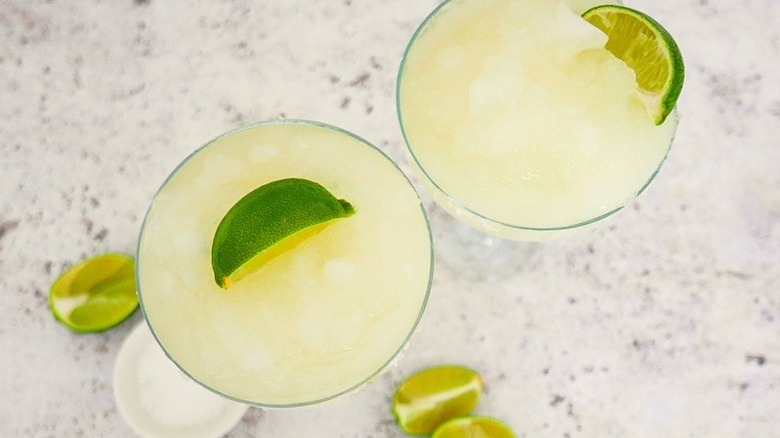 Two frozen margarita cocktails in glasses with lime wedges