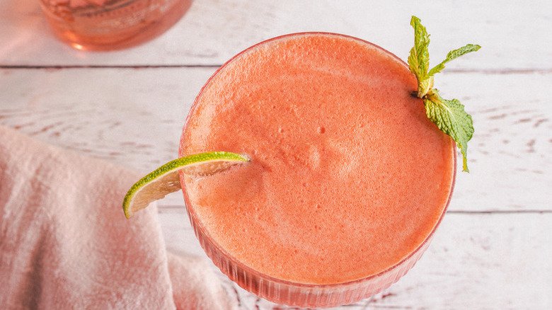Frozen watermelon cocktail in glass with lime wedge and mint sprig garnishes