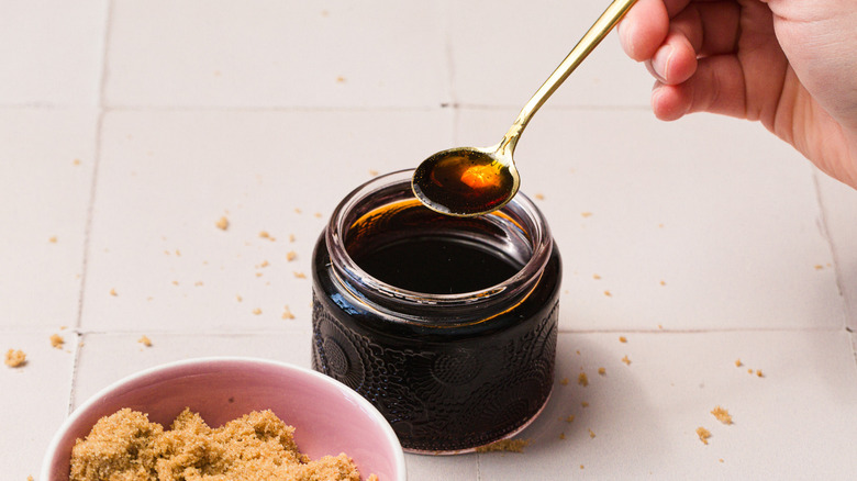 Hand lifting a spoon of syrup over a jar