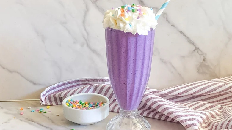 DIY Deluxe Grimace Shake in a tall milkshake glass garnished with whipped cream and sprinkles