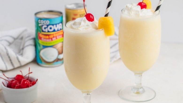 Two piña colada cocktails garnished with whipped cream, pineapple, and maraschino cherries