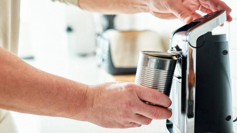 Person using electric can opener in kitchen