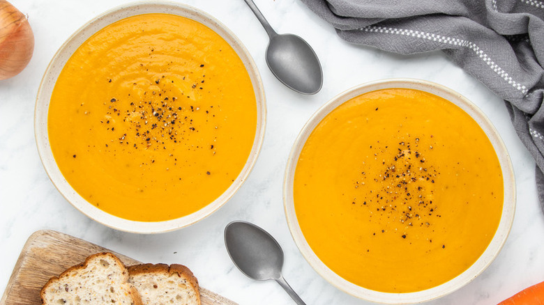 Two bowls of carrot and butternut squash soup, garnished with cracked black pepper