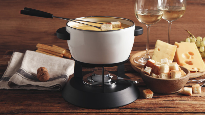 Cheese fondue pot over mini stove, next to chunks of bread and cheese