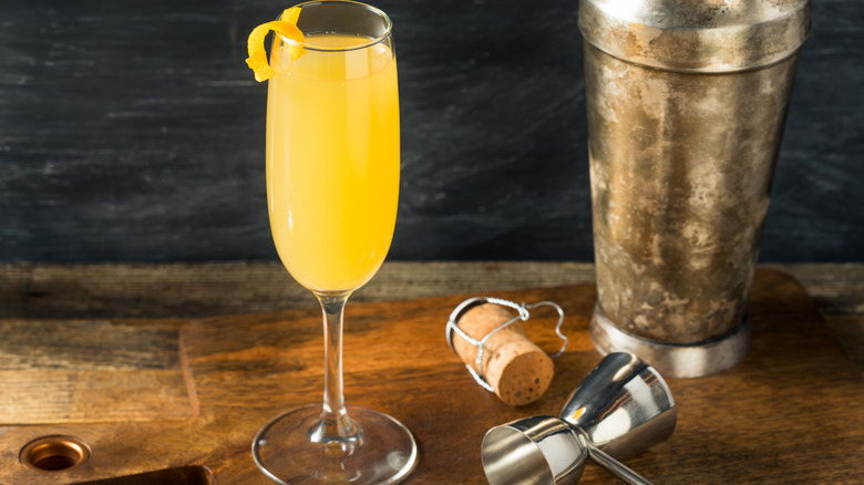 Classic French 95 cocktail with an orange twist beside a shaker and cork
