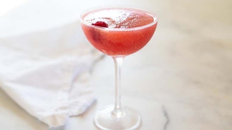 Pink frozen cocktail in glass with fresh raspberry garnish