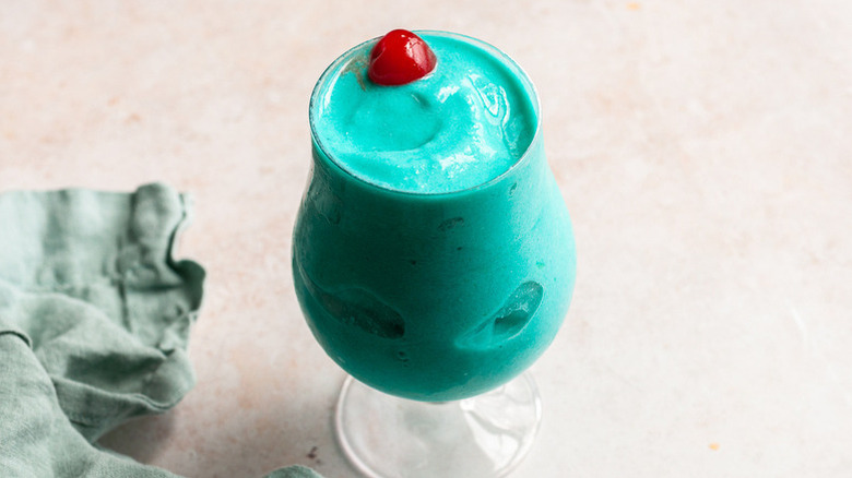 Frozen blue Hawaiian cocktail in glass with cherry garnish
