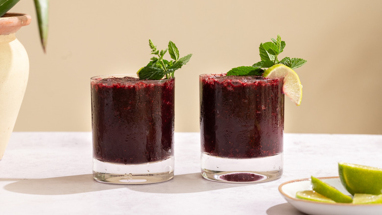 two cups of frozen blueberry mojitos with mint leaves and lime wedges