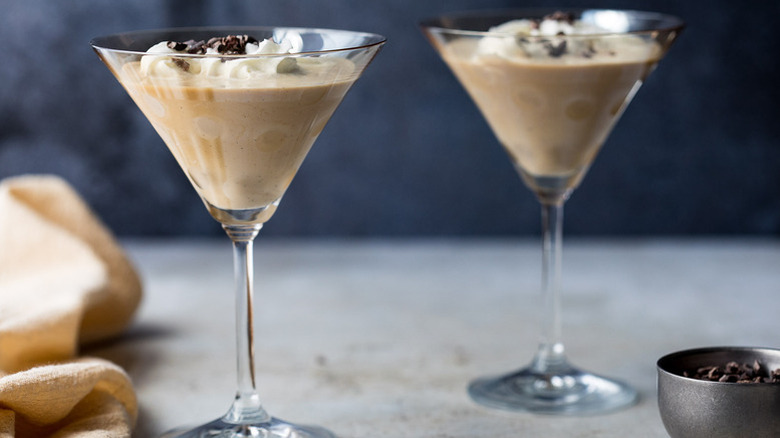 Two frozen brandy cocktails garnished with whipped cream and cacao nibs