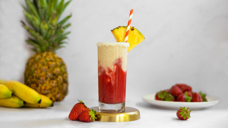 Two tone banana and strawberry cocktail in glass with pineapple wedge garnish