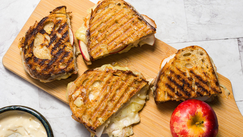 Four grilled apple turkey cheddar sandwich halves with an apple
