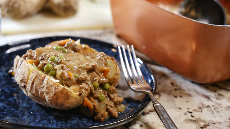 split jacket potato filled with beef and vegetables in gravy with a fork next to it on a blue plate