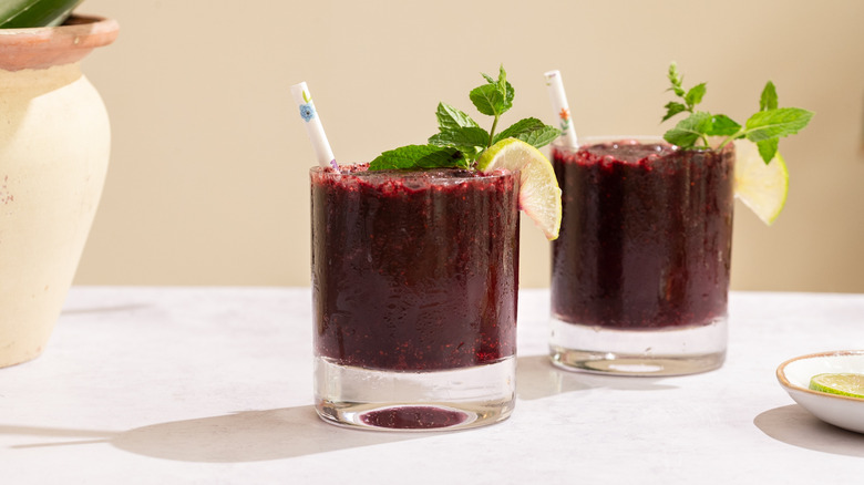 two glasses of frozen blueberry mojito with straws, mint leaves, and lime wedges