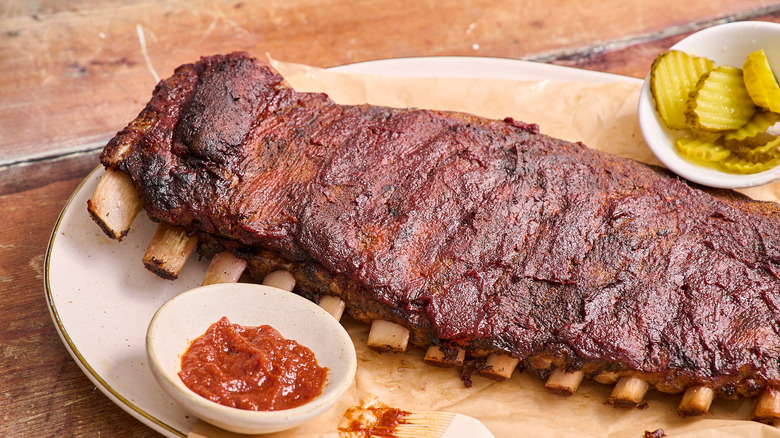 St. Louis-style ribs on a platter with sauce and pickles on the side