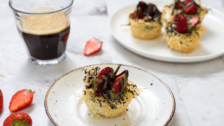 Dubai chocolate strawberry cup on small plate with coffee and more treats in background