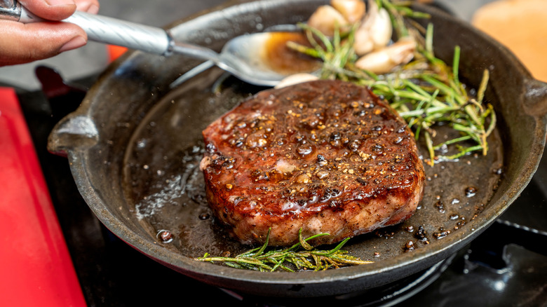 steak cooking in cast iron pan with rosemary garlic and fat