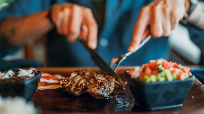 Man using fork and knife to cut steak at restaurant