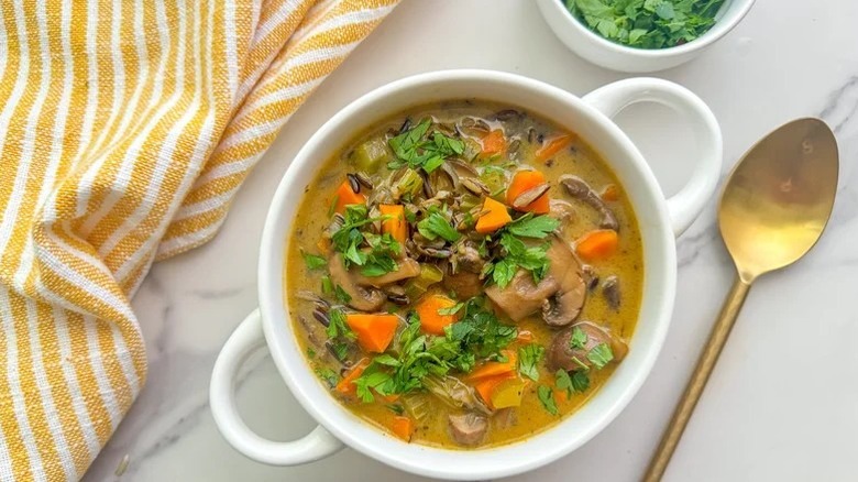 Wild rice soup with mushrooms and carrots in bowl next to napkin and spoon