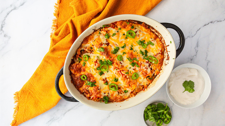 Enchiladas besides bowls of jalapeno and sour cream