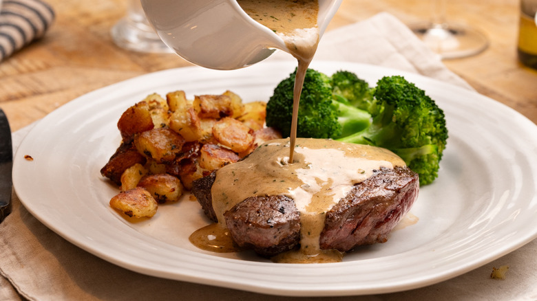 Gravy pouring onto steak on plate with potatoes and broccoli