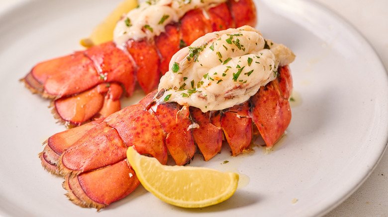 butterflied lobster tails on a plate with lemon wedge