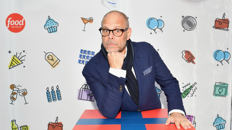 Alton Brown looks forward at a Food Network event with a backdrop behind him