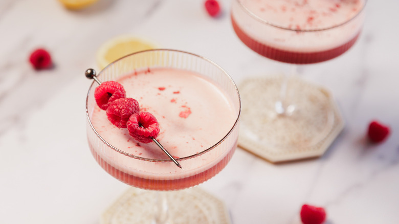 Two cocktail glasses with raspberries and lemon slices all around