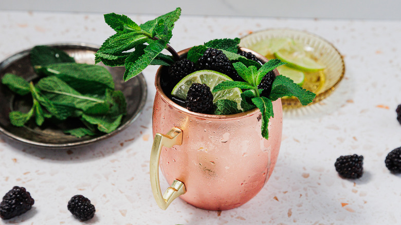 A frosted copper glass of a Kentucky mule with a garnish of mint leaves, blackberries and lime wedges