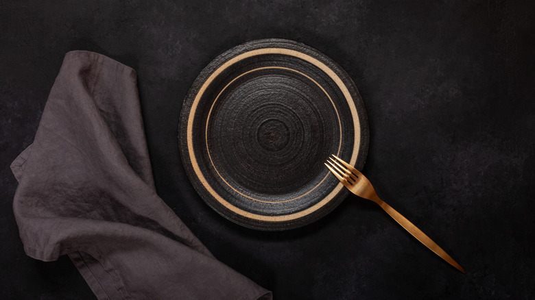 Empty ceramic plate and fork on black background