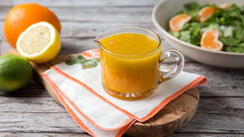 Citrus vinaigrette in serving cup surrounded by citrus fruits and salad