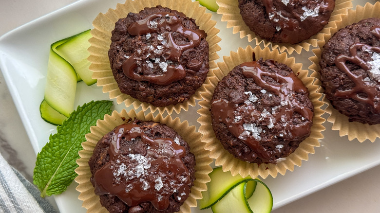 Chocolate zucchini muffins on white plate with zucchini strands
