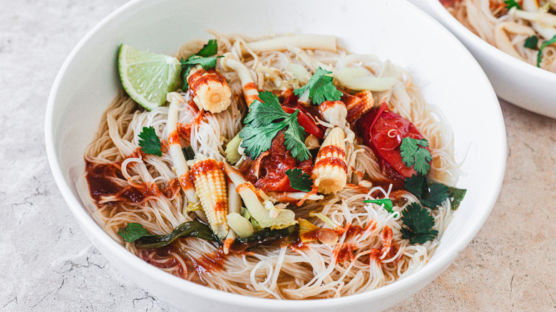 Bowl with spicy chicken noodle soup, topped with Sriracha, cilantro, and lime wedges