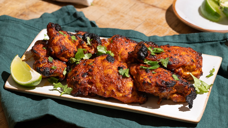Charred pollo asado on platter with lime wedge and herbs