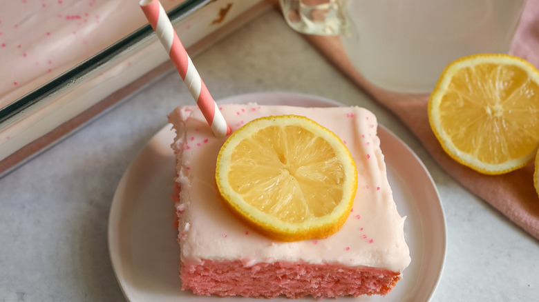 Pink frosted cake with lemon garnish and straw