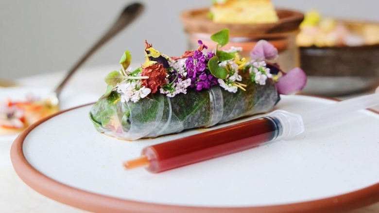 Duck sel dish by chef Donald Young featuring a spring roll decorated with flowers and soup in a syringe