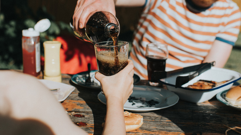 Man pouring soda for friend across table