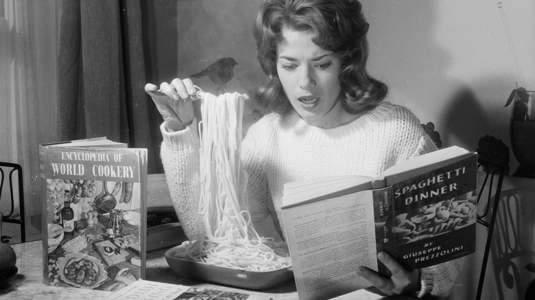 woman eating spaghetti surrounded by cookbooks in the '60s