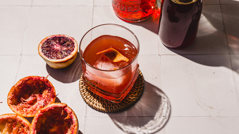 Overhead view of glass with blood orange screwdriver cocktail alongside empty blood orange peels and bottles