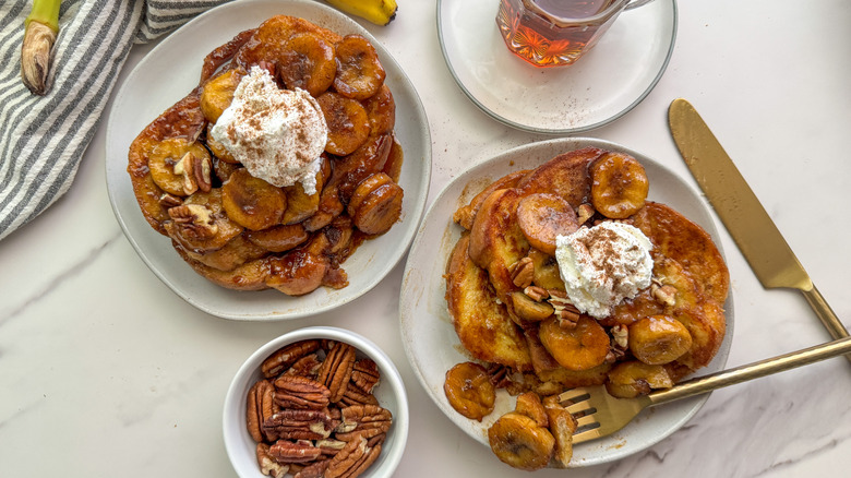 two plates of French toast with bananas Foster on top and a side of pecans