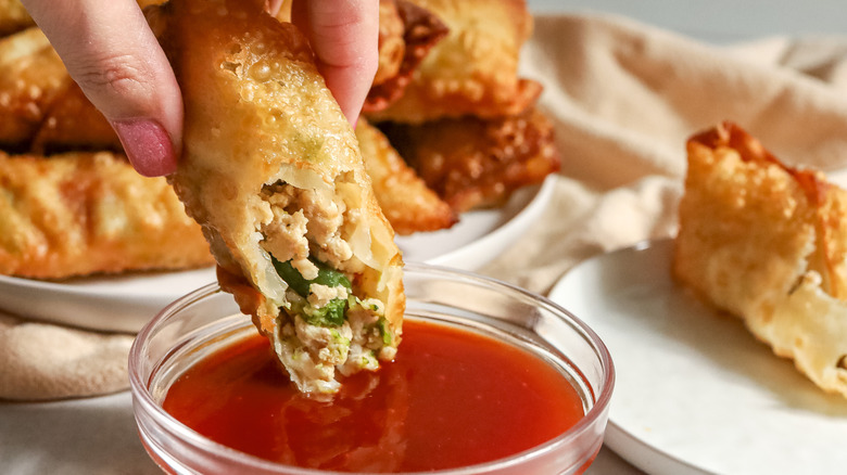 hand dipping egg roll in red sauce