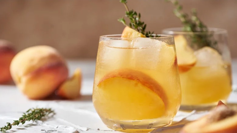 Summertime peach whiskey smash in glasses with ice, peaches, and thyme